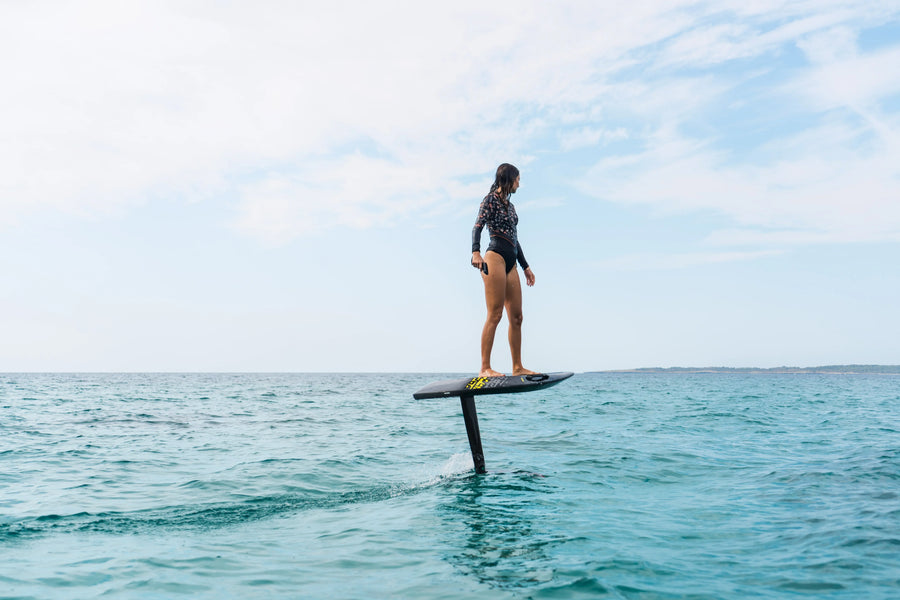 Rider on an Aerofoils Performance eFoil scanning the open horizon over calm water, remote control in hand before making a go or no-go call