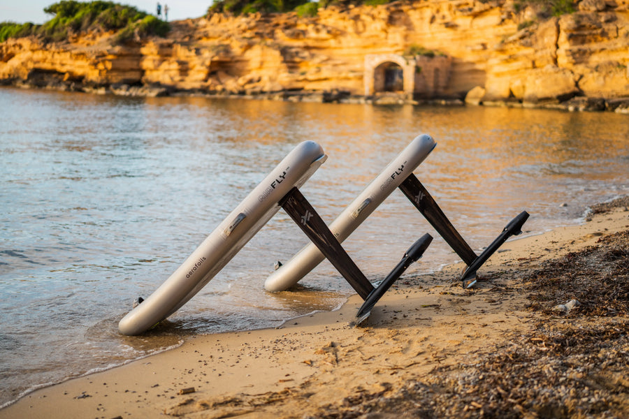 Two Aerofoils Airfly boards propped up on a Mallorca beach at golden hour, mast-down and ready to be packed up for transport